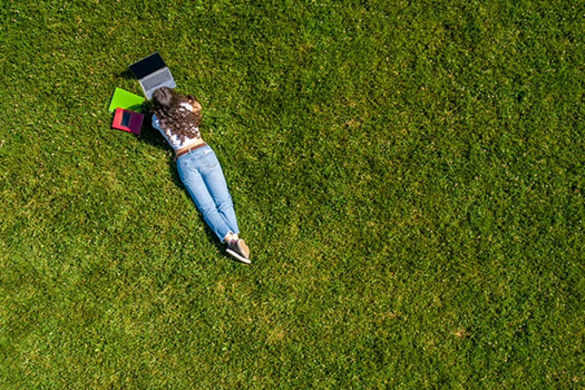 Student working on computer while lying down in grass