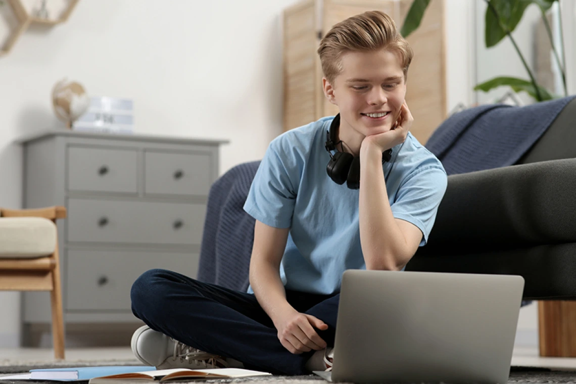 Estudiante sentado en el suelo de su casa trabajando en una computadora portátil