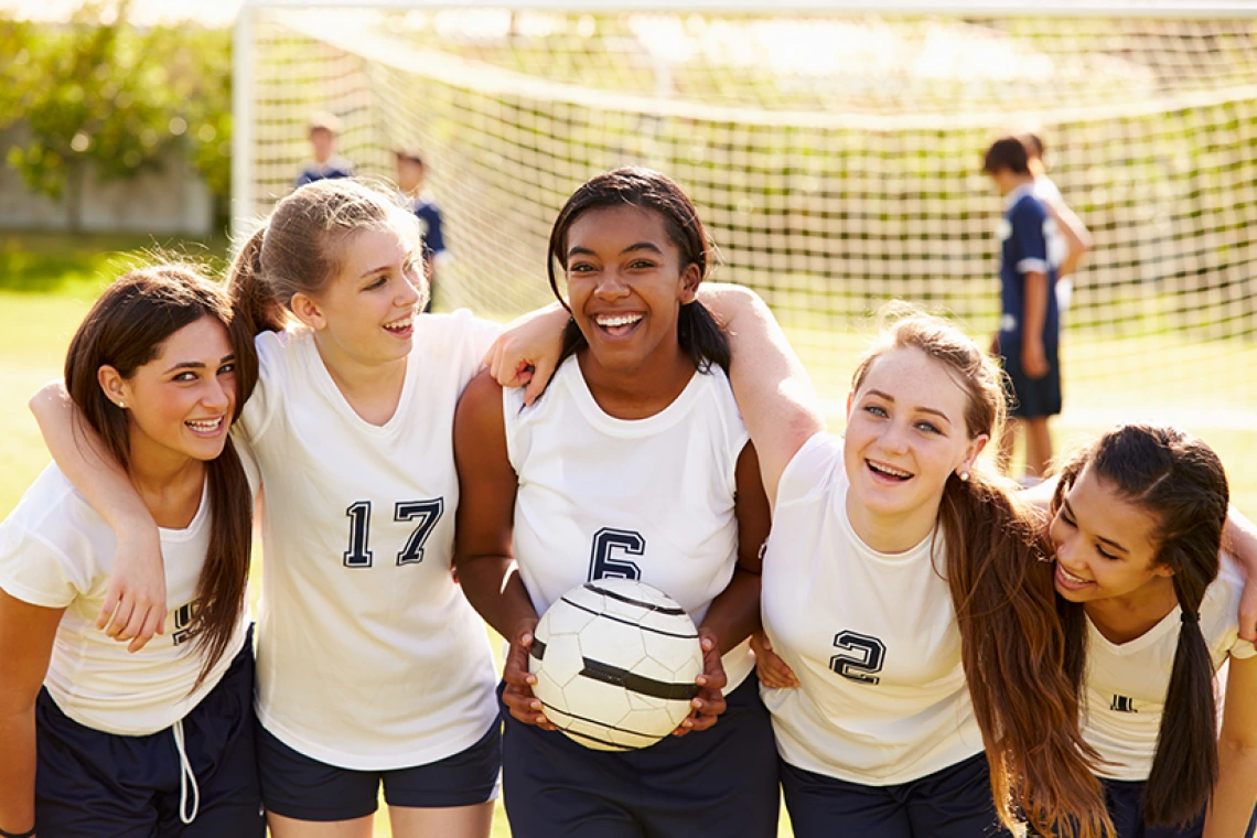 Grupo de chicas de secundaria con uniformes de fútbol sonriendo juntas