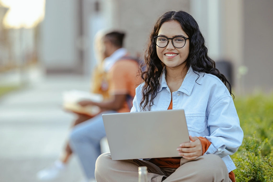 Student holding laptop and smiling outside