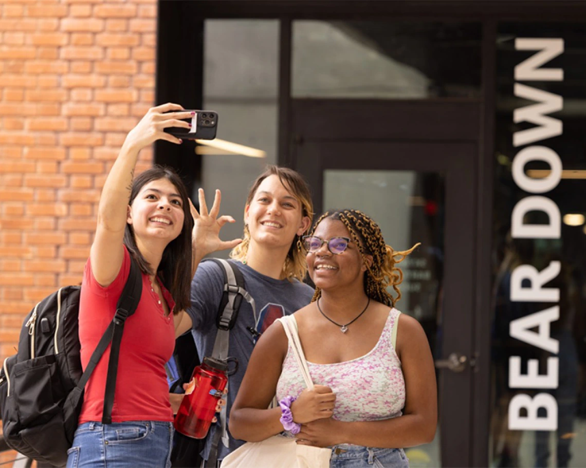 Three students taking a selfie outside of a UA campus building