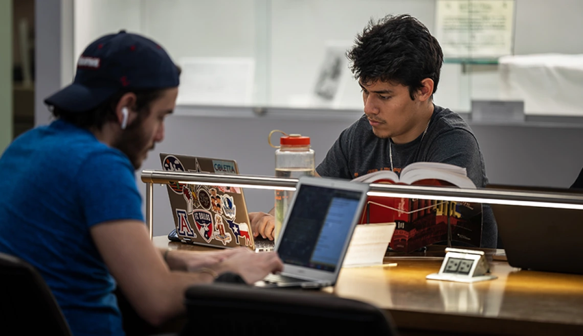 Dos estudiantes que estudian en computadoras portátiles en la biblioteca